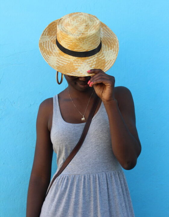 black woman tilting hat, in front of blue wall